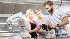 Three students review a piece of machinery