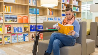 A single female SRH student sits and reads in a library