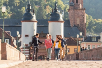 Five students walking across a bridge with a backdrop of beautiful historic buildings in Germany.