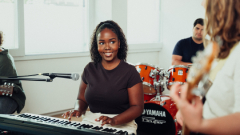 A female student sits at her keyboard looking at the guitarist as they play